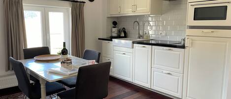 Una cocina moderna con armarios blancos, encimera negra y zona de comedor con mesa y sillas.