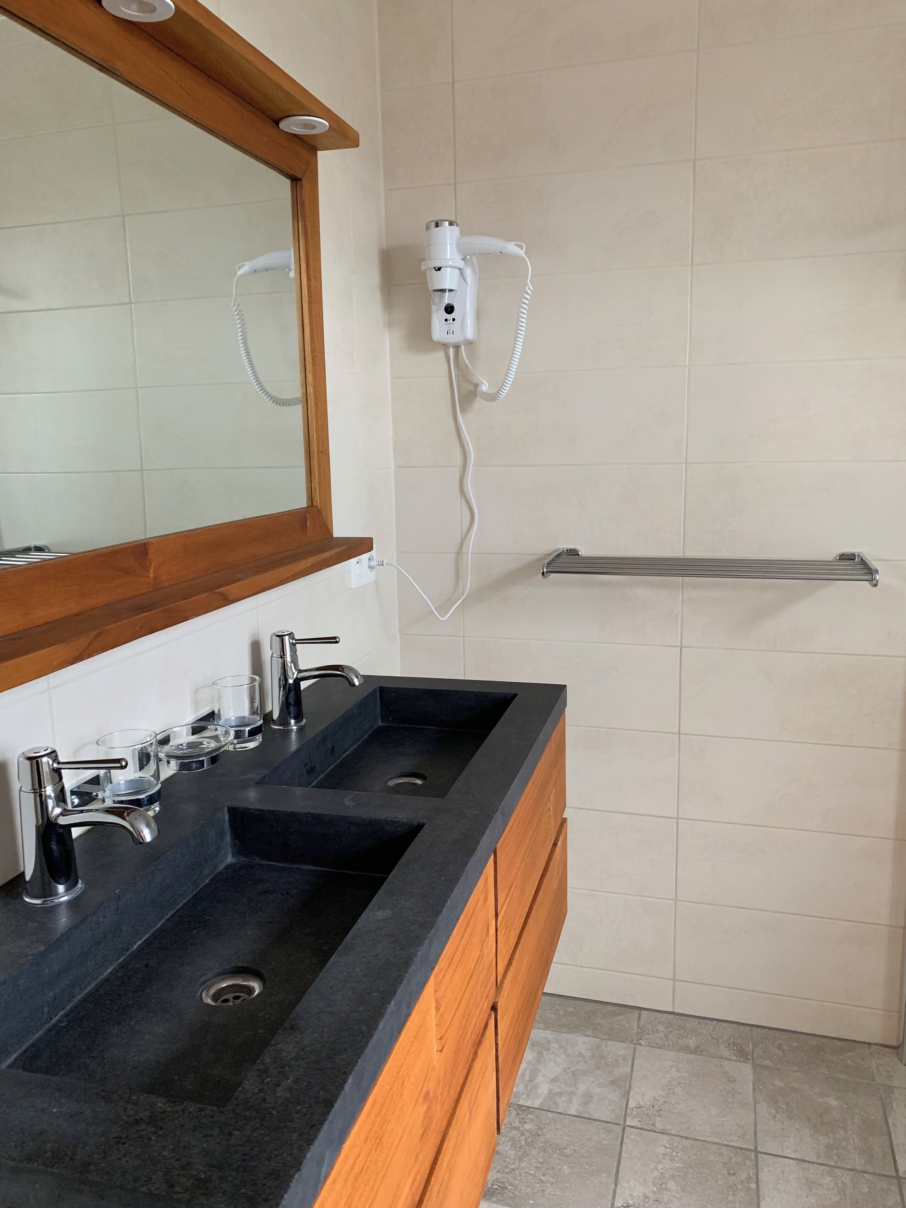 A bathroom with a black sink, two faucets, a mirror, a towel rack, and a hairdryer mounted on the wall.