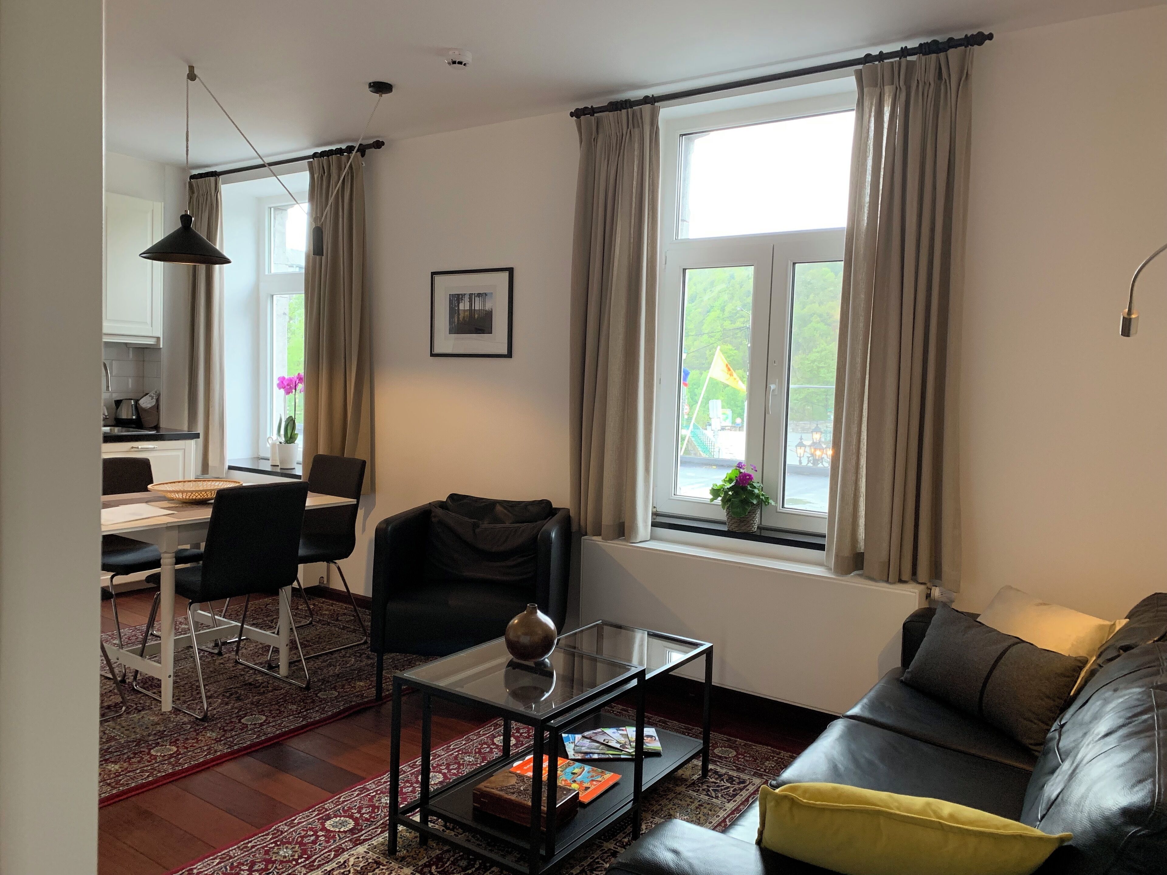 A living room with a sofa, a glass coffee table, a dining table with chairs, and a window with curtains.