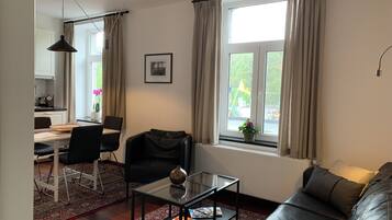 A living room with a sofa, a glass coffee table, a dining table with chairs, and a window with curtains.