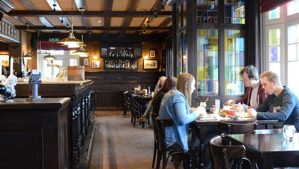A restaurant interior with wooden beams, bar area, and patrons dining. - Le Baron Suites & Apartments (Stavelot)