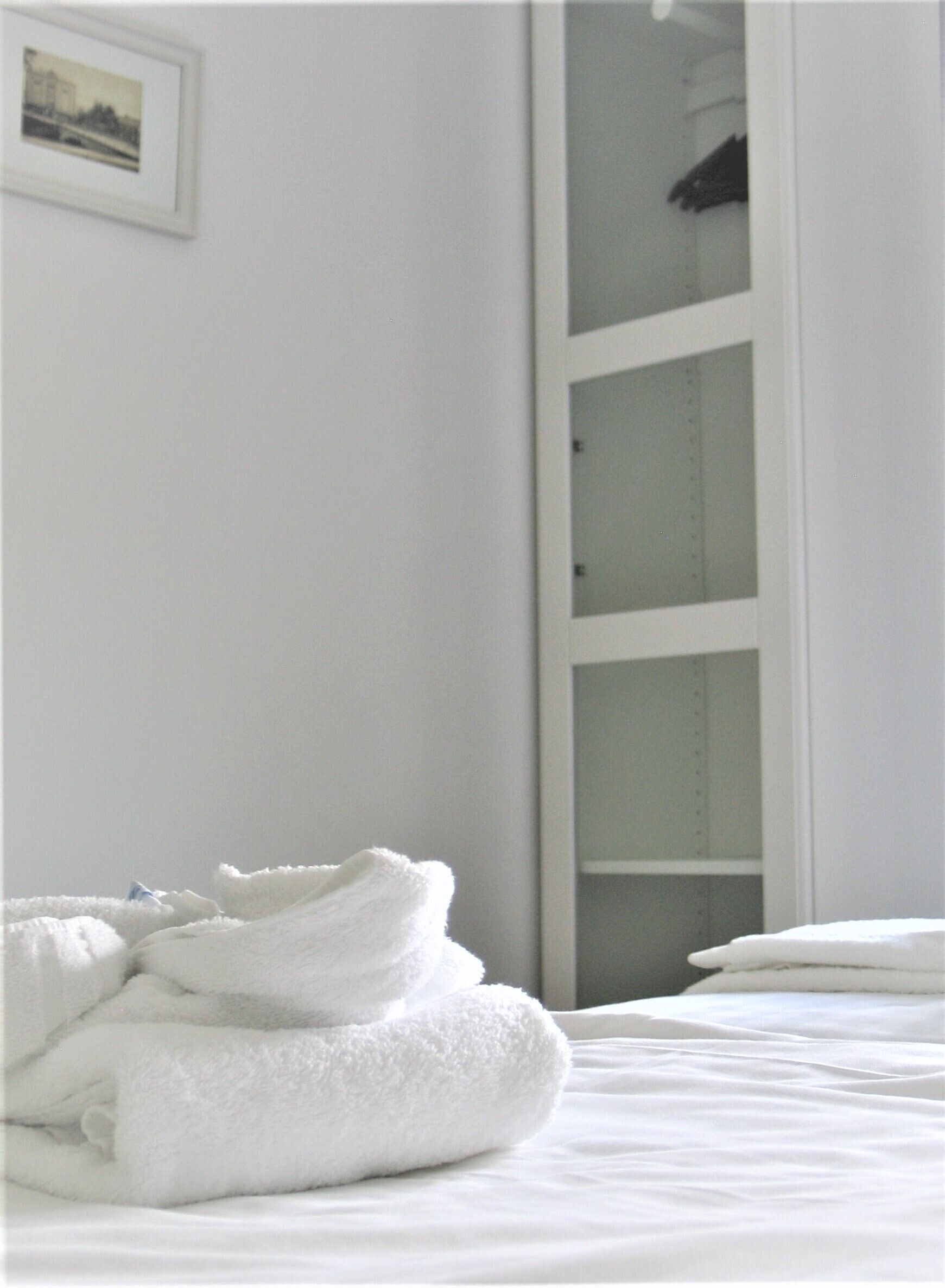 A neatly made bed with white linens and a stack of folded towels.