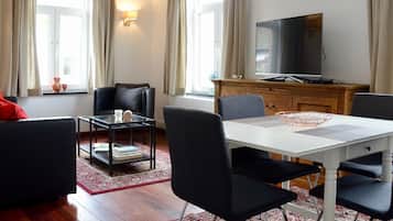 Un salon moderne avec une table à manger blanche, des chaises noires, un canapé noir avec des coussins rouges, une table basse en verre, un meuble en bois et un téléviseur à écran plat.