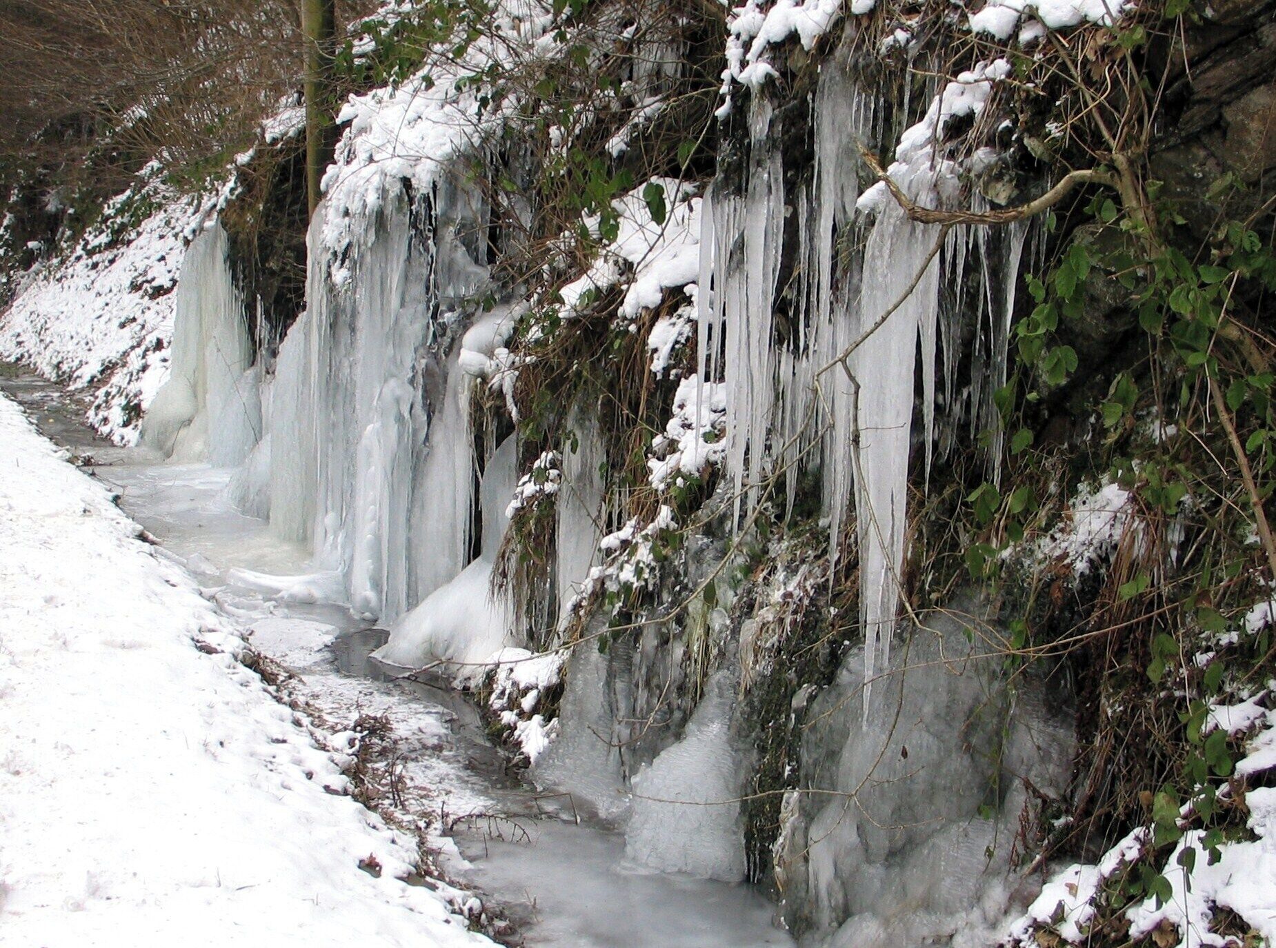 Un río helado con estalactitas colgando de las orillas, rodeado de vegetación cubierta de nieve.
