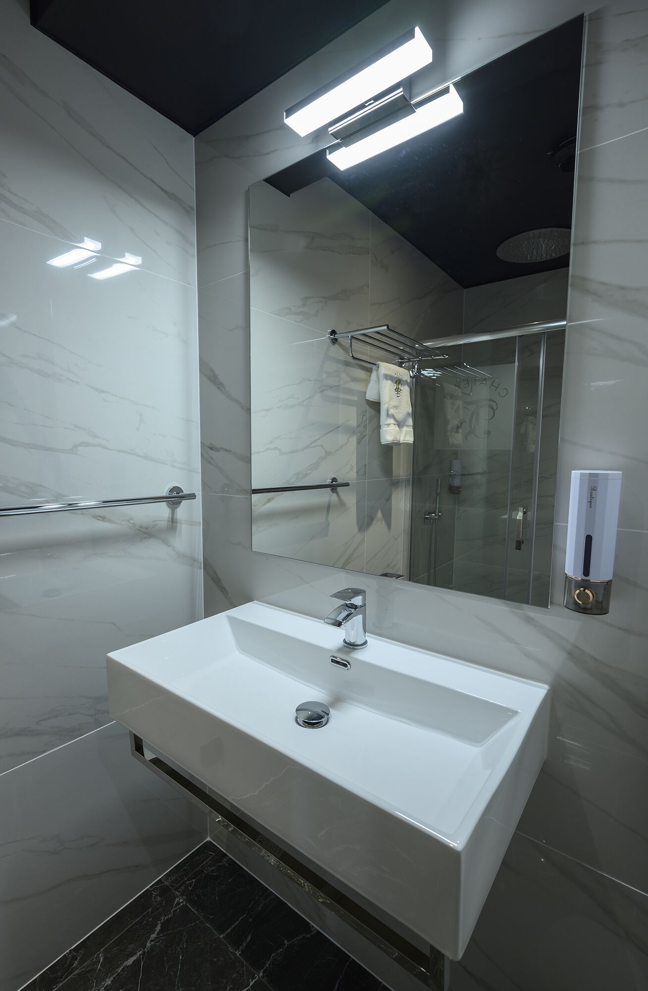 A modern bathroom with a large mirror, a white sink, and a glass shower enclosure.