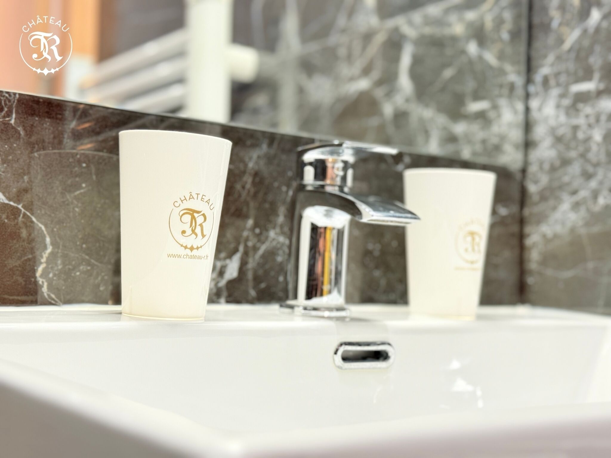 A bathroom with a white sink, a chrome faucet, and two white cups with a logo on them.