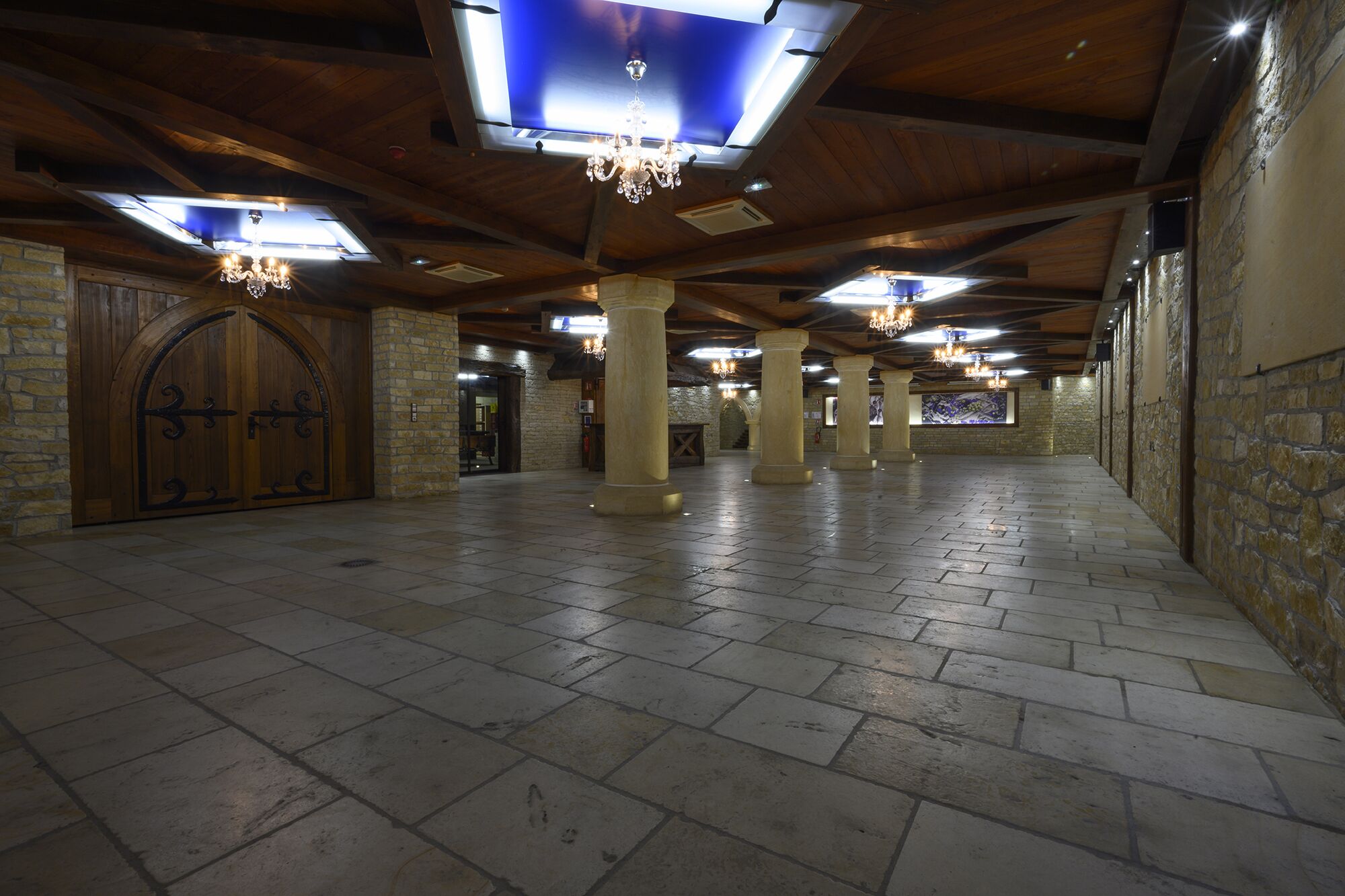 A spacious hall with stone walls, wooden beams, and columns.