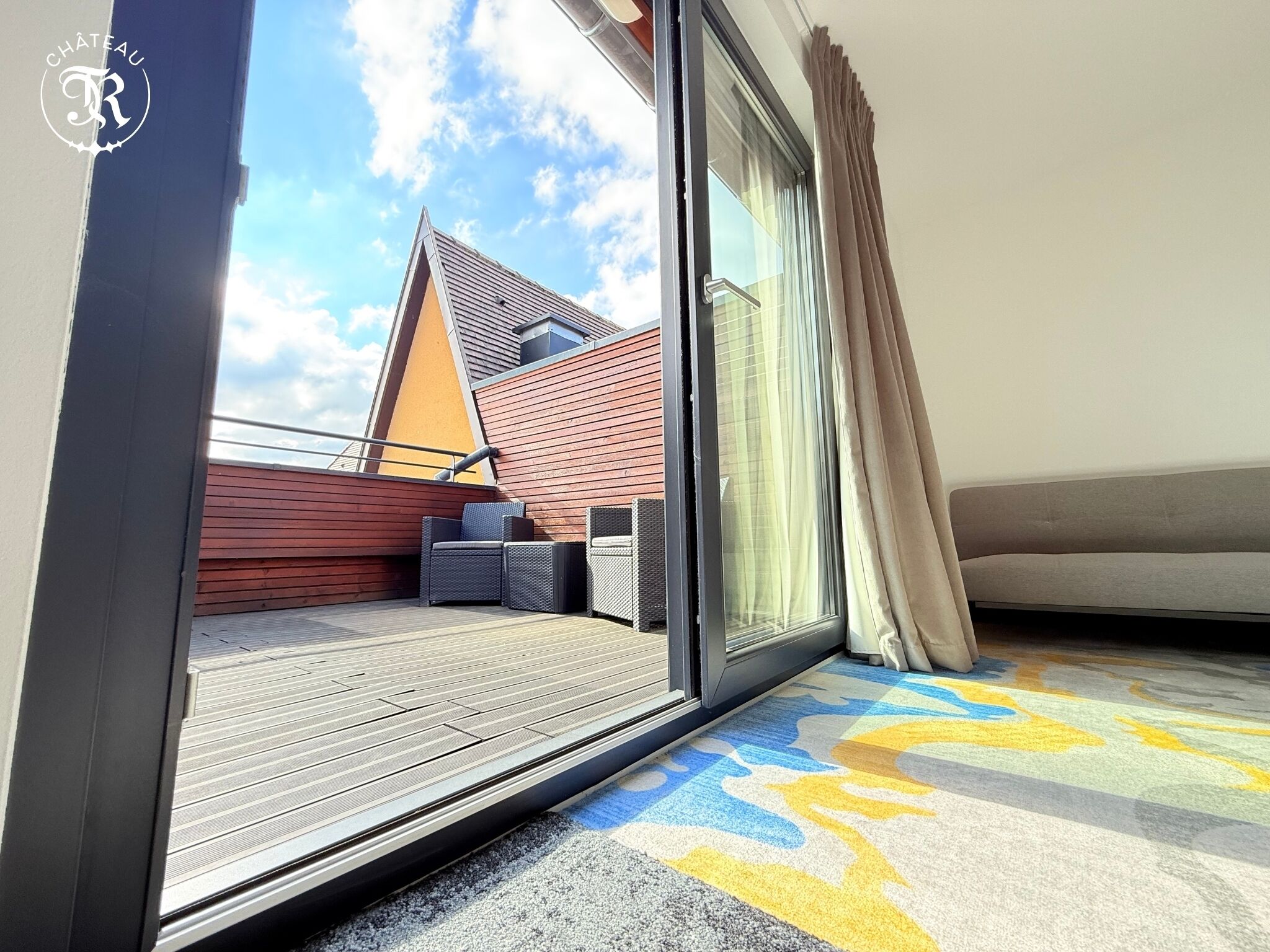 A balcony with a wooden deck, a sofa, and a chair.