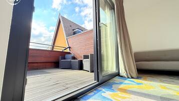 A balcony with a wooden deck, a sofa, and a chair.