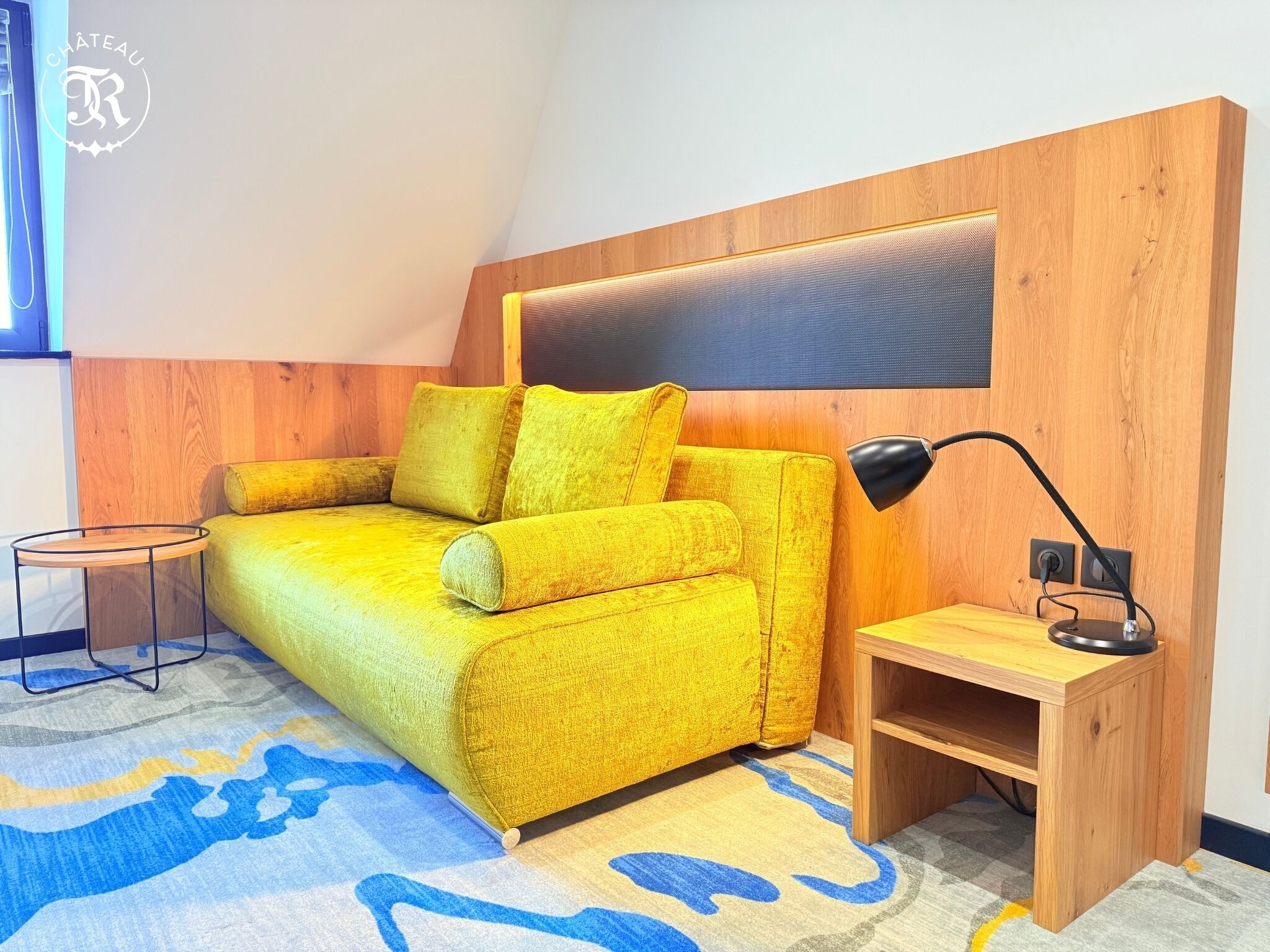 A room with a yellow sofa, a small wooden side table, and a lamp.