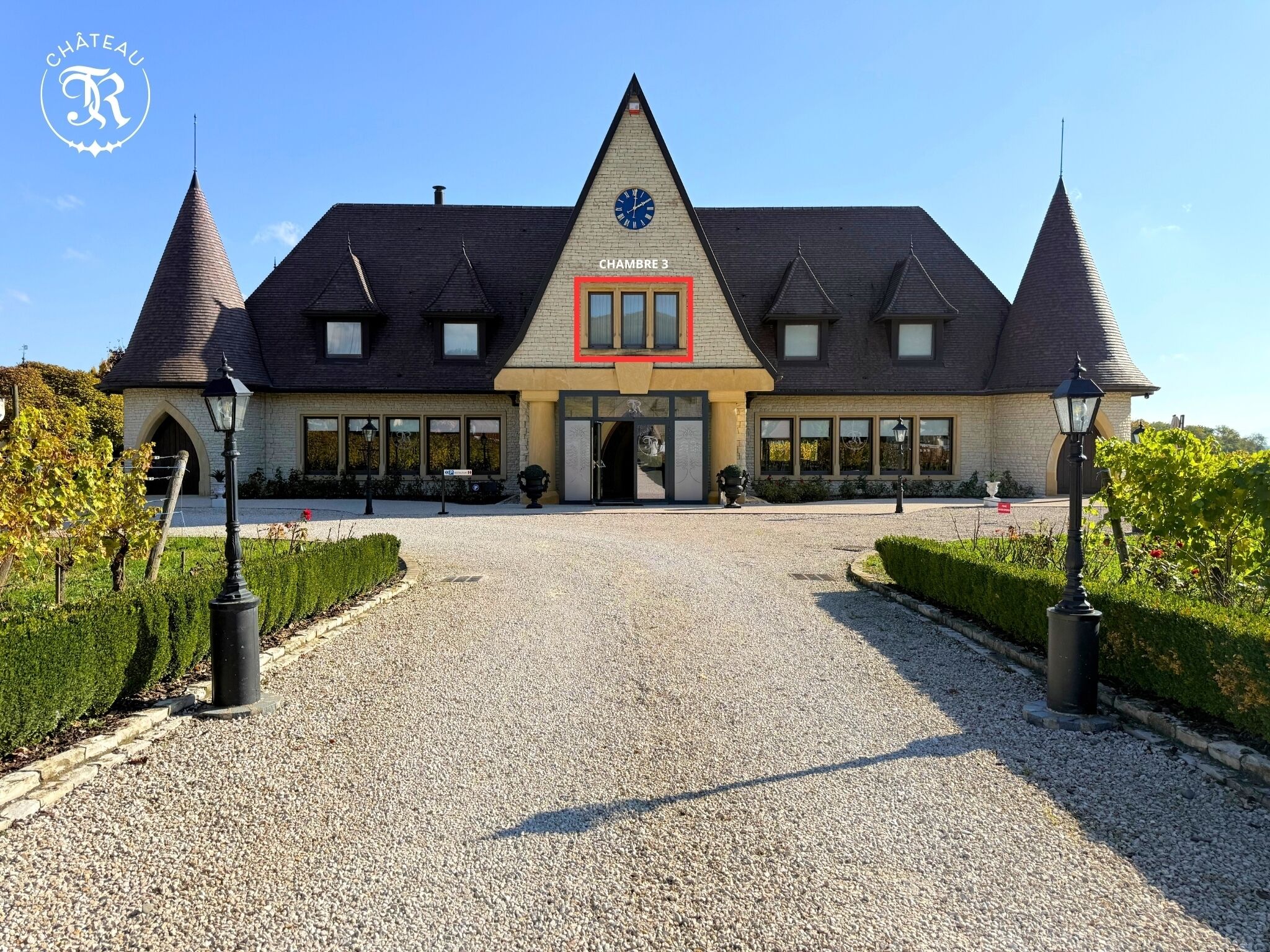 A château with a clock tower, a gravel driveway, and a red-framed entrance.