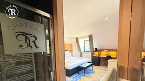 Una habitació d'hotel amb un llit, una taula de treball i una finestra. Hi ha un cartell a la porta que diu "CHÂTEAU".