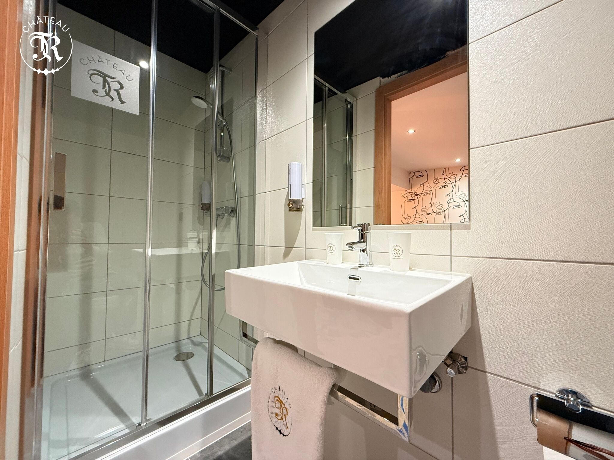 A modern bathroom with a glass shower enclosure, a white sink, and a mirror with a decorative frame.