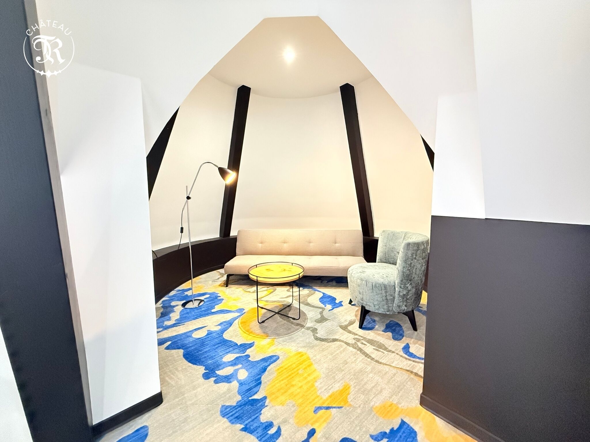 Une chambre de style loft moderne, avec un plafond haut, un canapé, un fauteuil et un tapis à motifs.