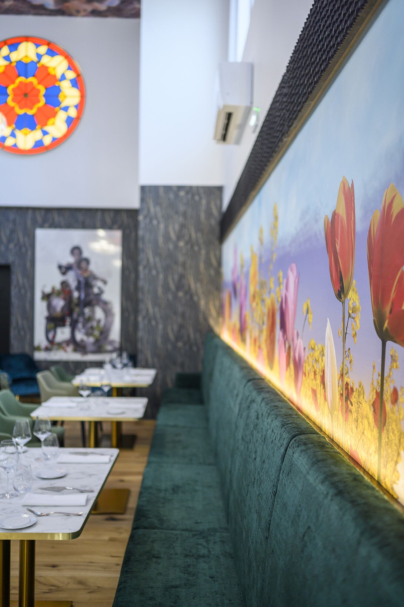 A restaurant with a long counter, green upholstered seating, and a mural of flowers on the wall.