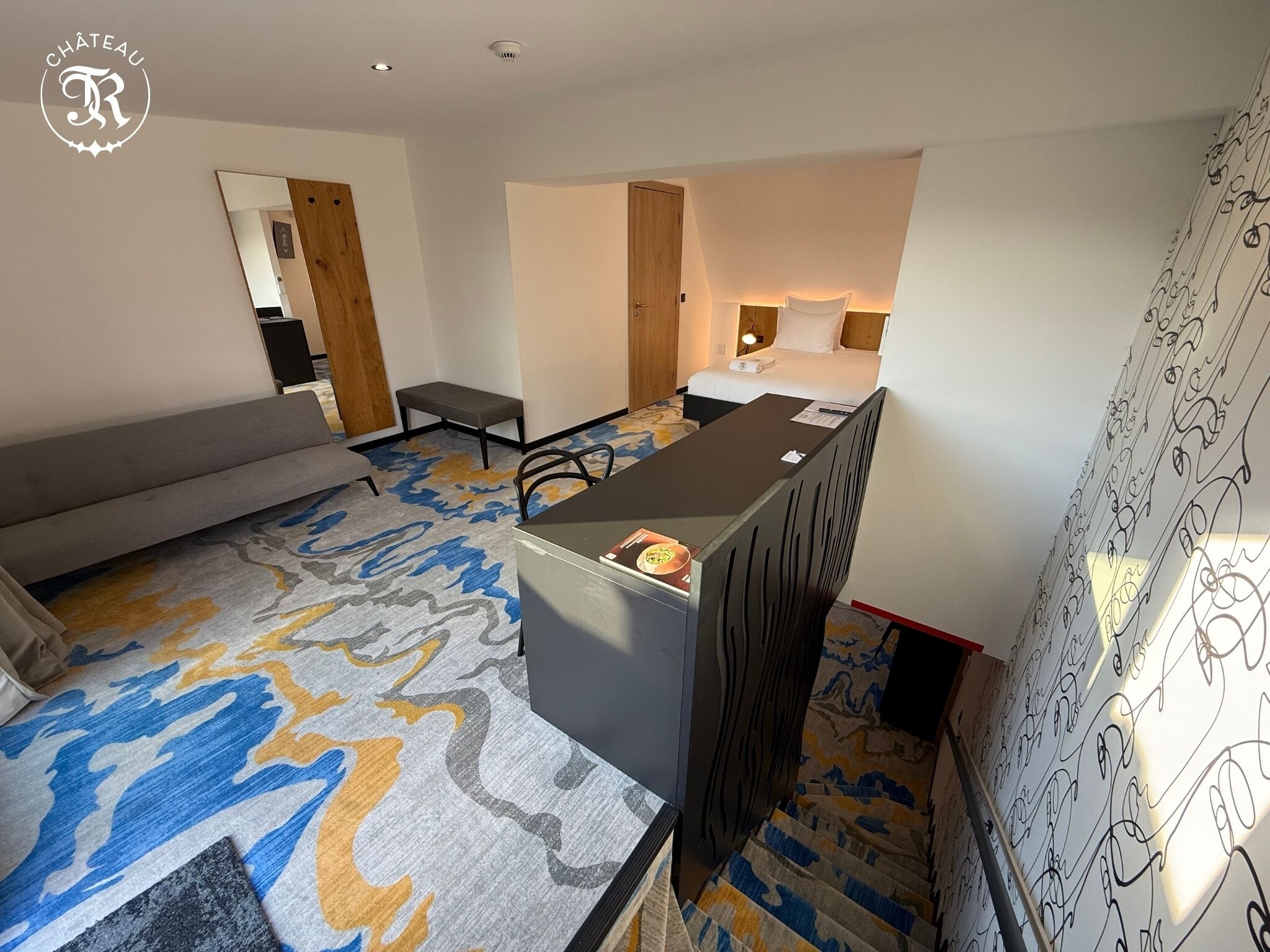 A hotel room with a bed, a desk, a sofa, and a patterned carpet.