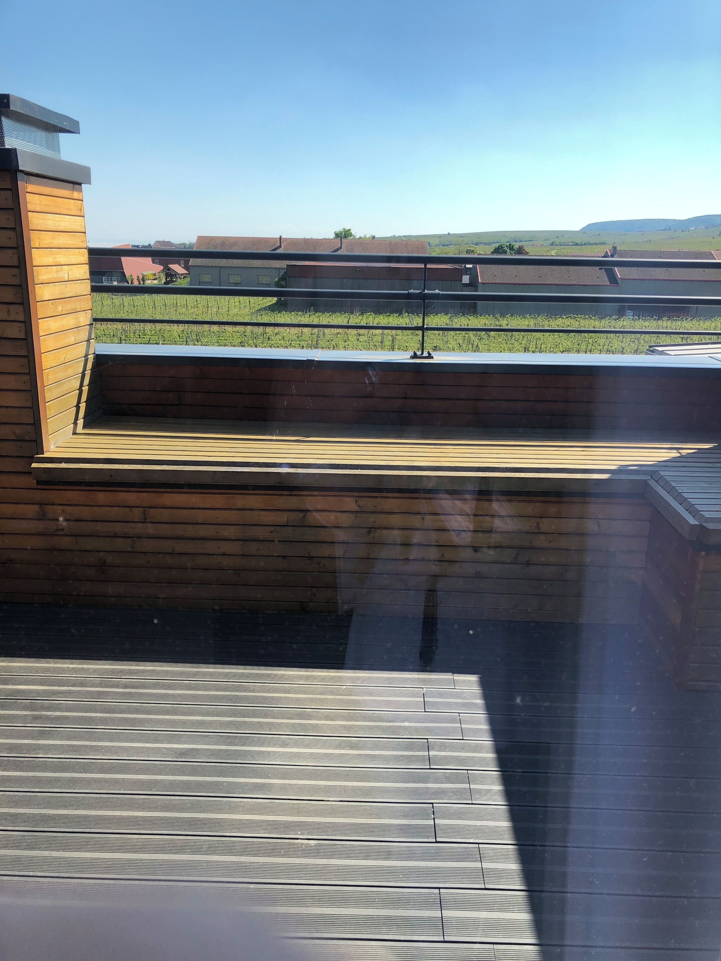 Una terraza de madera con vistas a un viñedo y edificios al fondo.
