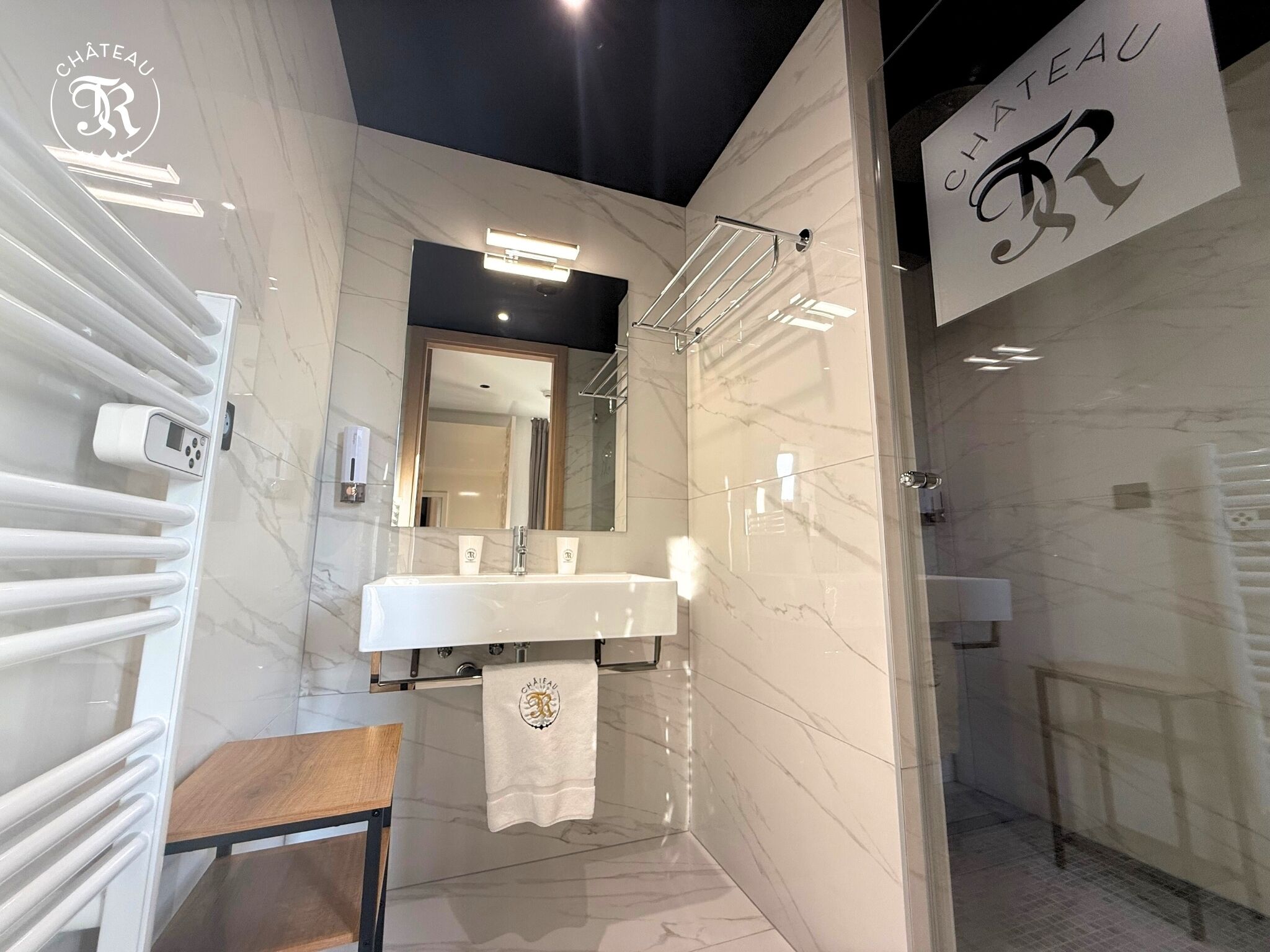 A modern bathroom with a marble floor, a large mirror, a white sink, and a glass-enclosed shower.
