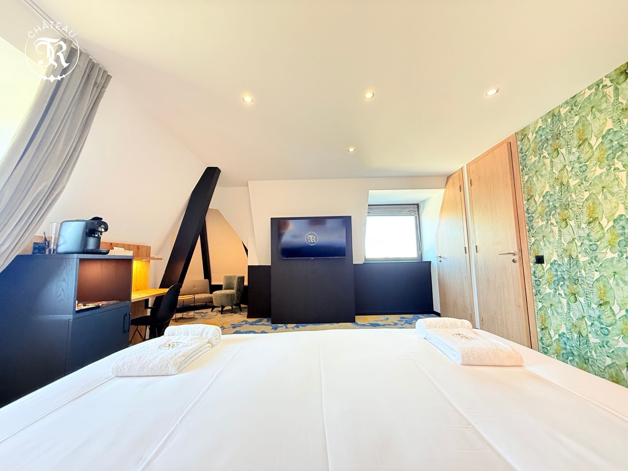 A modern hotel room with a large bed, a desk with a coffee machine, a TV, and a window with a view.