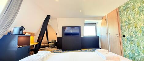 A modern hotel room with a large bed, a desk with a coffee machine, a TV, and a window with a view.