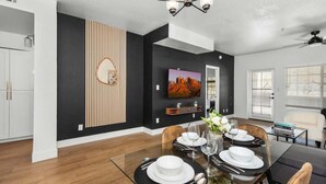 A modern dining area with a glass table set for four, a black and white color scheme, and a large painting on the wall.