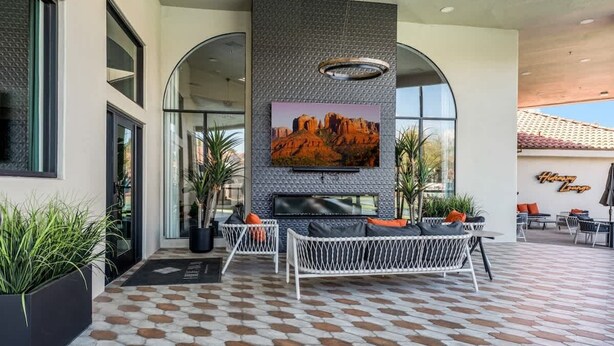 A modern outdoor seating area with a large TV screen, comfortable seating, and a patterned floor.
