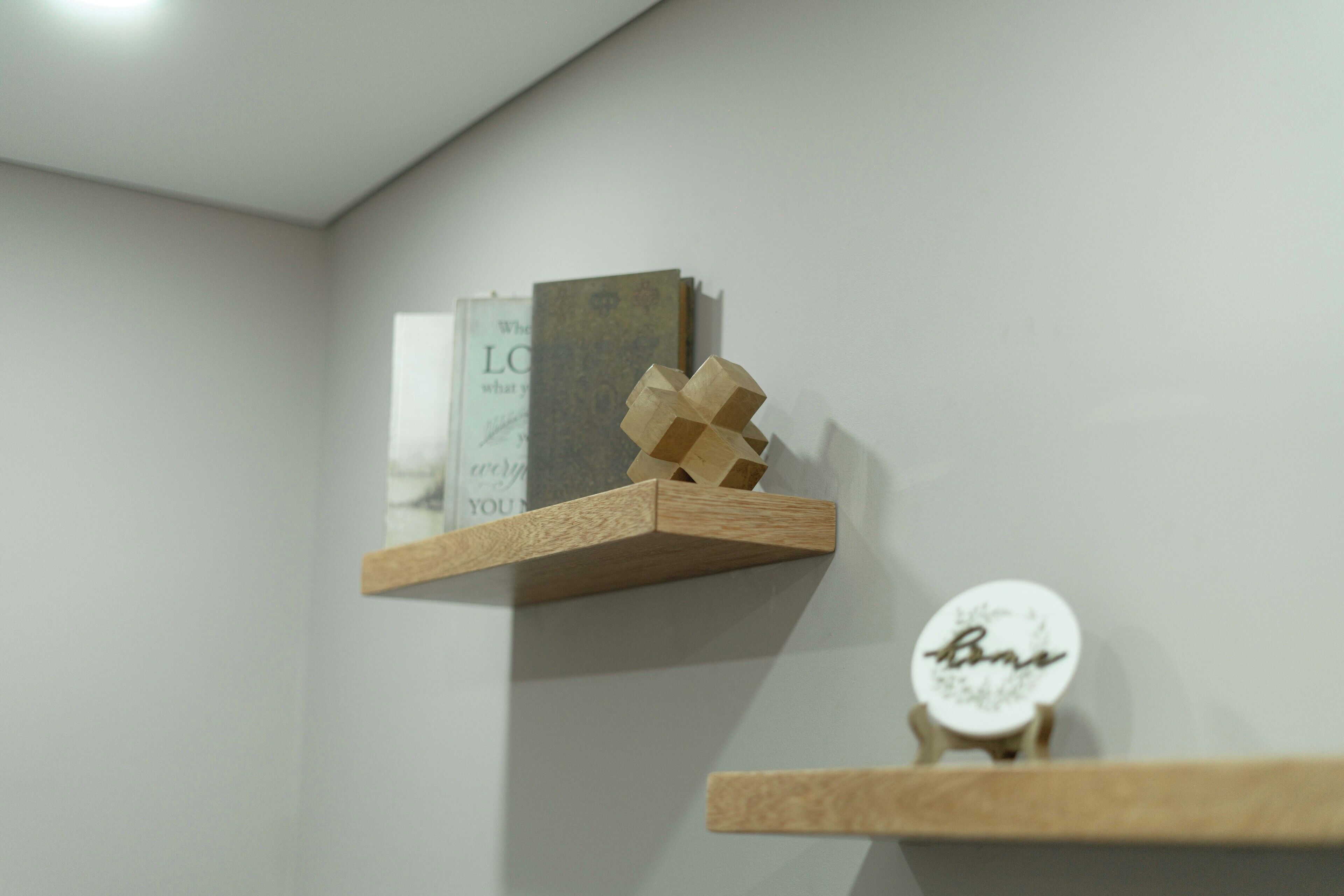 Ein schlichter Raum mit zwei Holzbögen, einer mit einem Buch und einer geometrischen Holzskulptur, der andere mit einem runden Schild.