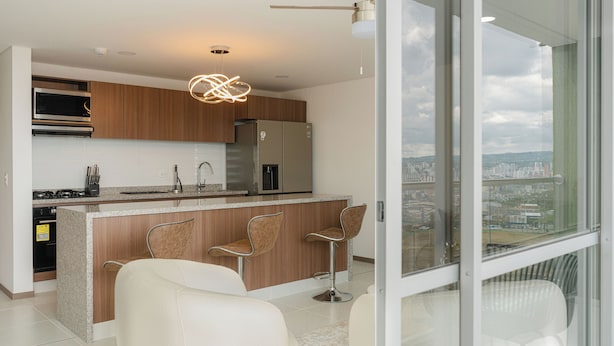 A modern kitchen with a central island, stainless steel appliances, and a city view through large windows. - Matiz 1701 (Dosquebradas)