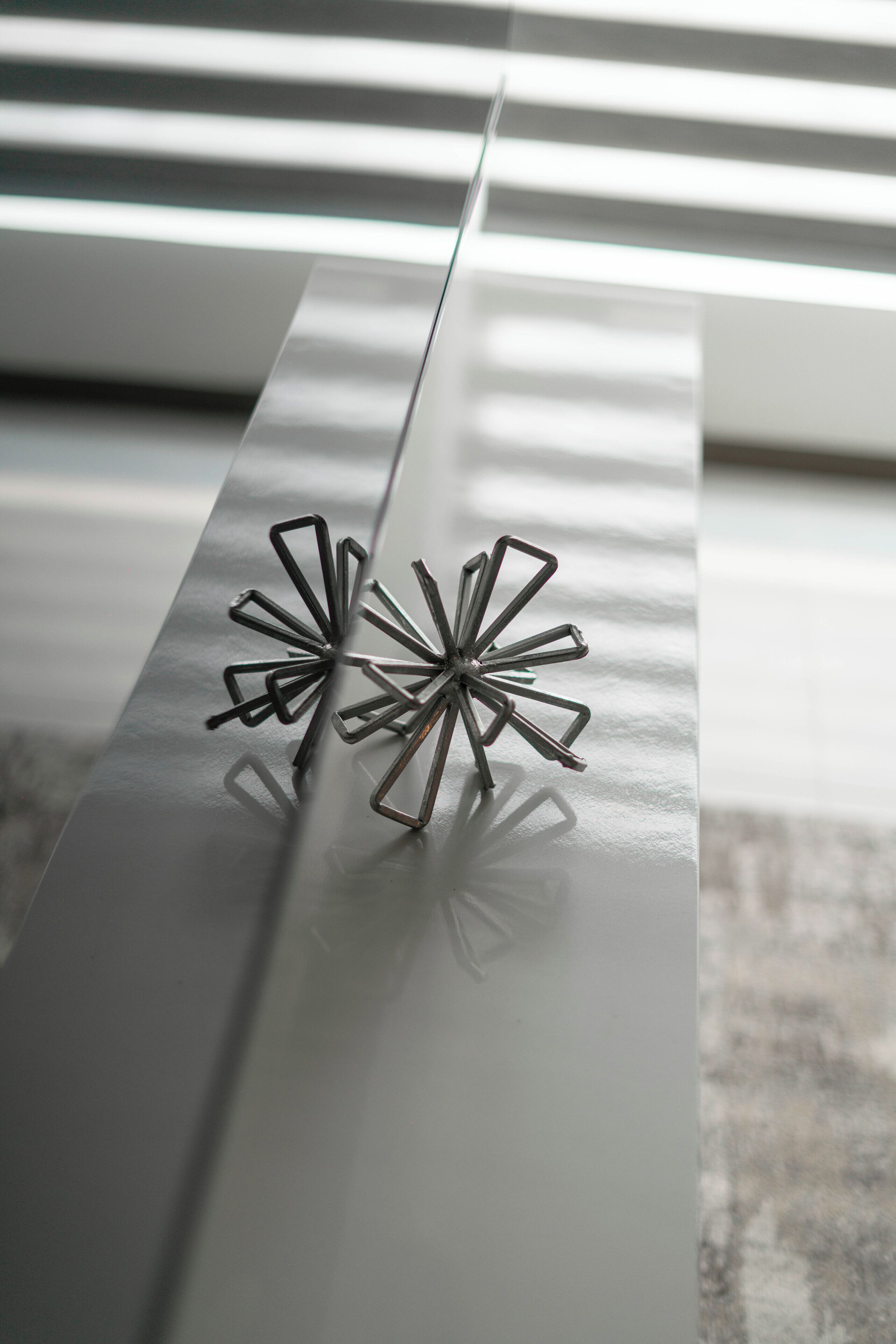 Une sculpture abstraite en métal, placée sur une surface réfléchissante.