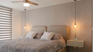 A modern bedroom with a large bed, a ceiling fan, bedside lamps, and a nightstand with a vase. - Matiz 1701 (Dosquebradas)