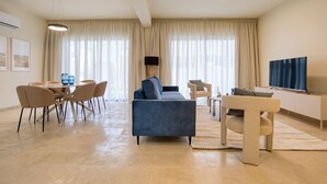 A modern living room with a sofa, chairs, a TV, and a dining area with a table and chairs. - Avalon Gardens Villa 13 (Emba)