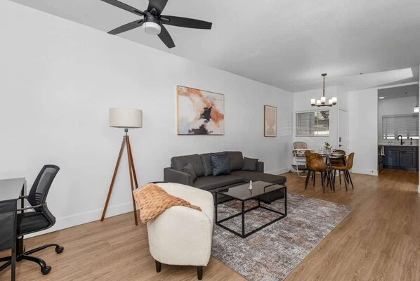 A modern living room with a gray sofa, a white armchair, a coffee table, and a dining area with a chandelier.