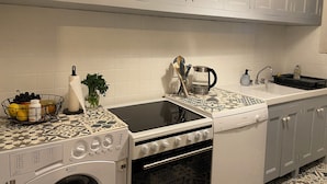 A kitchen with white cabinets, a washing machine, an oven, and a coffee maker.