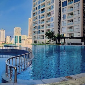 A modern residential building with a swimming pool, surrounded by other high-rise buildings.
