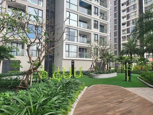 A modern apartment building with multiple balconies, a well-maintained garden, and outdoor exercise equipment.