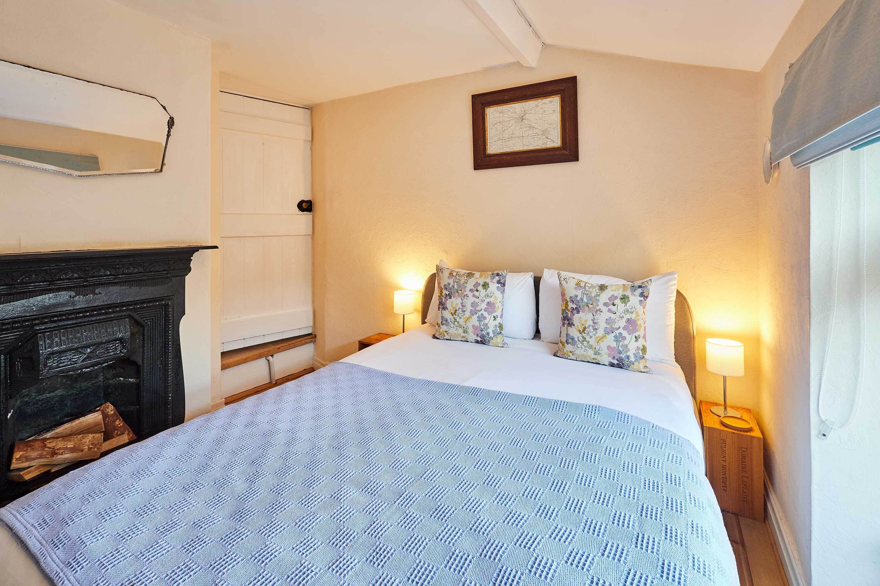 A bedroom with a bed, a fireplace, and a wall-mounted picture.