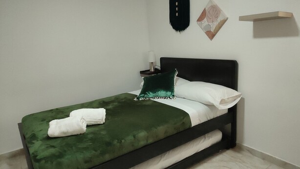 A neatly made bed with a green bedspread, white pillows, and a green throw pillow. There is a white towel folded on the bed. - Apto Sexta 103 (Pereira)