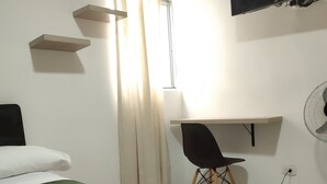 A hotel room with a bed, a desk, a chair, a TV, and a fan. - Apto Sexta 103 (Pereira)