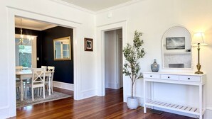 A room with a wooden floor, white walls, a dining table with chairs, a white console table with a lamp, and a potted plant. - White Lily Cottage, White Lily Cottage (St. Augustine)