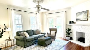 A living room with a green sofa, a grey armchair, a white fireplace, and a ceiling fan. - White Lily Cottage, White Lily Cottage (St. Augustine)