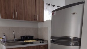A compact kitchen with wooden cabinets, a stainless steel refrigerator, a gas stove, and a sink. - Jardin 201 (Pereira)