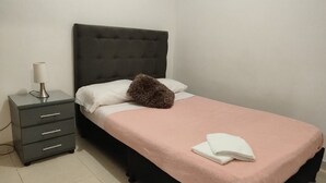 A single bed with a dark headboard, a bedside table with drawers, and a lamp. - Jardin 201 (Pereira)
