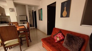 A living room with a red sofa, wooden dining table, chairs, and a kitchen in the background. - Jardin 201 (Pereira)