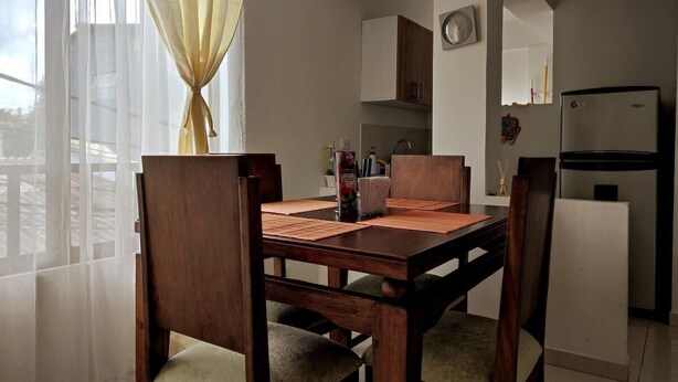 A dining area with a wooden table and chairs, a kitchen in the background, and a refrigerator. - Jardin 201 (Pereira)