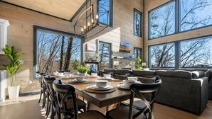 A modern dining area with a long table set for six, surrounded by black chairs with woven seats.