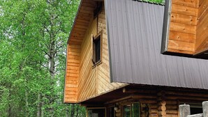 Una cabaña de troncos con terraza de madera y un letrero con el número 2, rodeada de árboles.