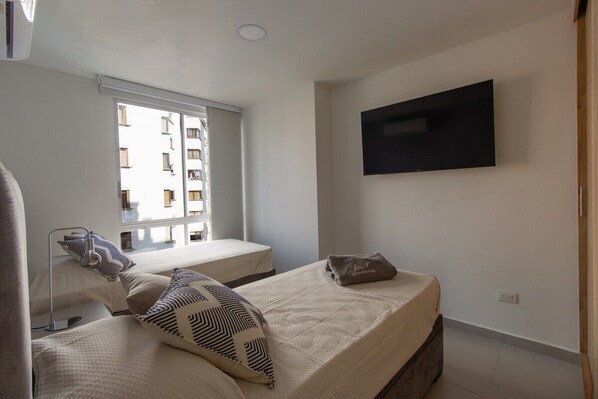 A bedroom with two beds, a TV mounted on the wall, and a window with a view of a building. - Oasis de Lujo para descansar en Pereira (Pereira)