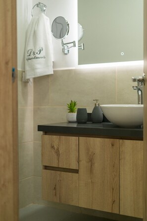 Een moderne badkamer met een houten wastafelmeubel, een witte wasbak en een kleine plant in pot.