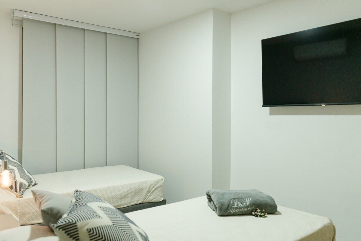 A hotel room with two beds, a flat-screen TV, and a window with blinds.
