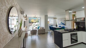 A modern kitchen with a central island, a dining area with blue chairs, and a living space with a sofa and a large mirror. - Oasis de Lujo para descansar en Pereira (Pereira)